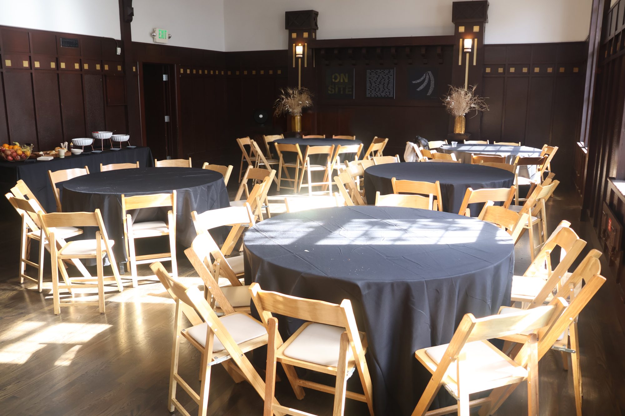 Banquet rounds with black linens and wooden chairs in a sunlit hall at Swedish American Hall