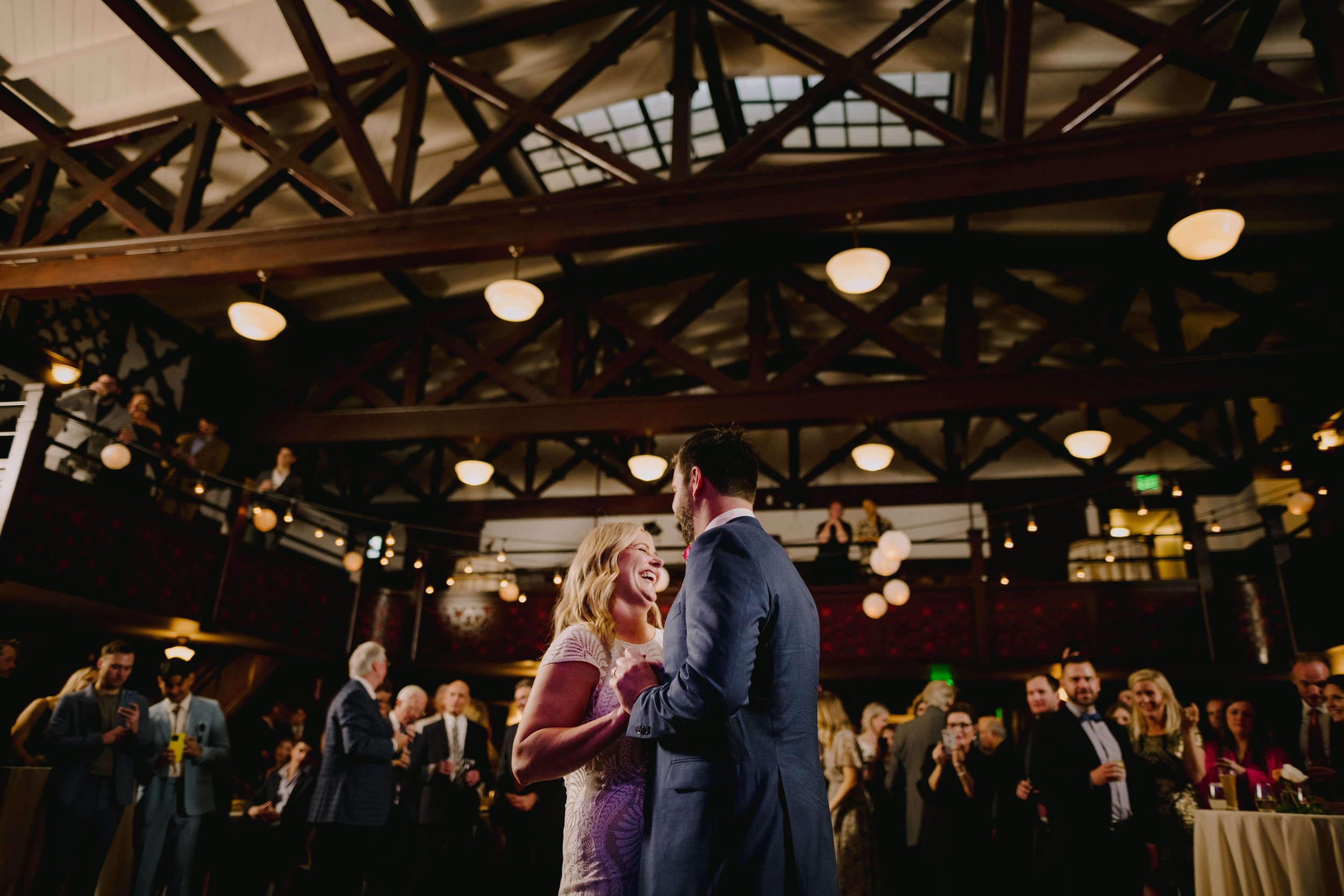 A couple dancing and smiling at a reception with guests in the background.